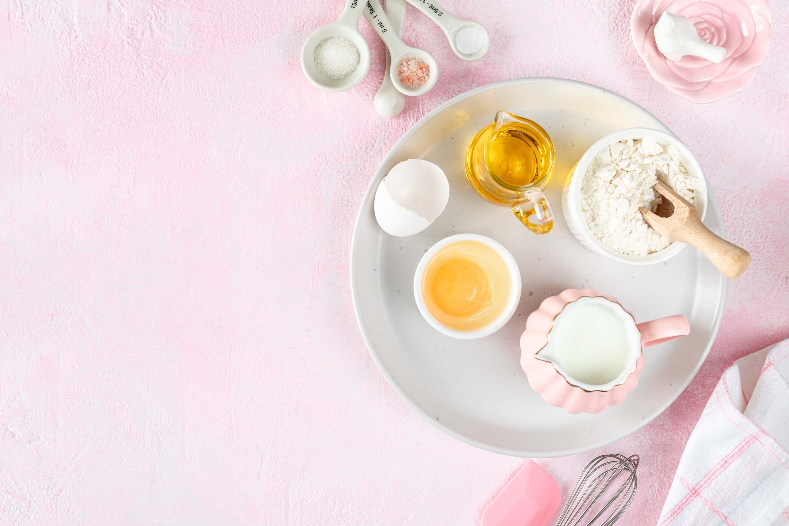 Baking ingredients and kitchen utensils on a pink background, top view. Butter, eggs, sugar, milk and flour for making dough.