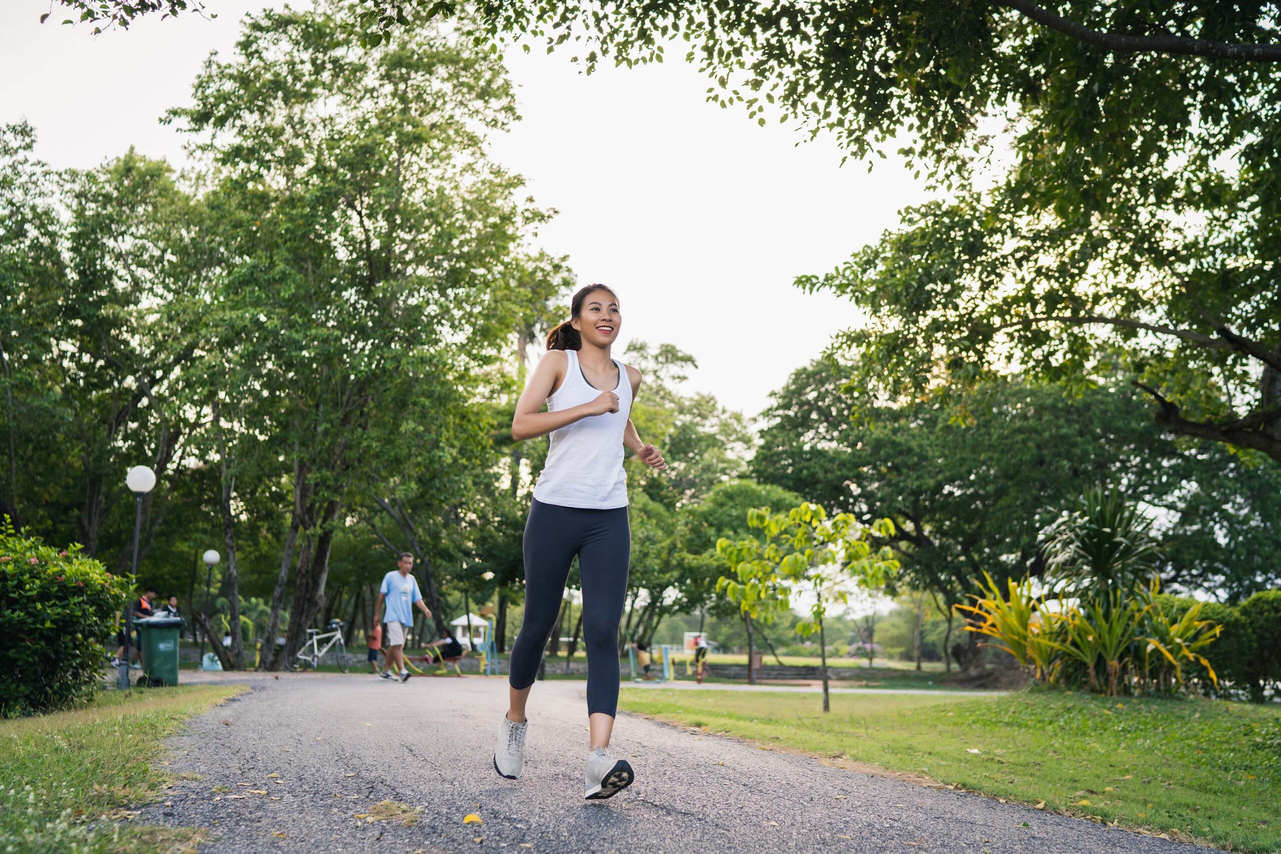 Healthy beautiful young Asian runner woman in sports clothing running and jogging on sidewalk near lake at park in the morning. Lifestyle fitness and active women exercise in urban city concept.