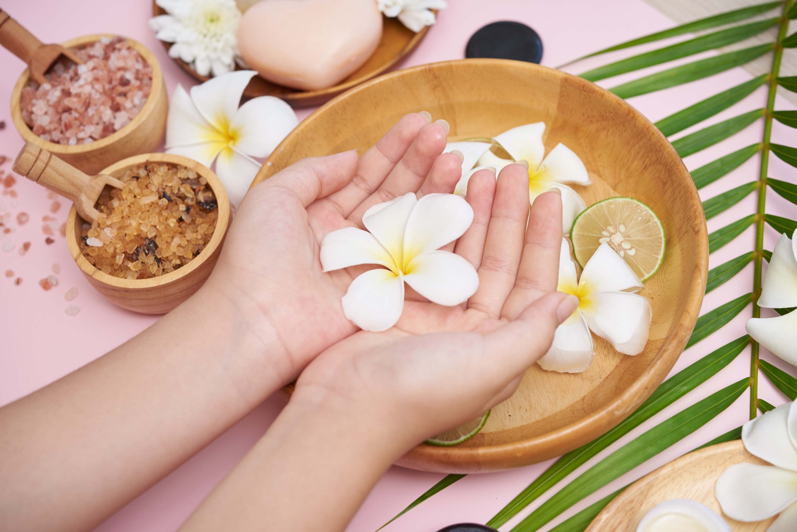 Woman soaking her hands in bowl of water and flowers, Spa treatment and product for female feet and hand spa, massage pebble, perfumed flowers water and candles, Relaxation. Flat lay. top view.